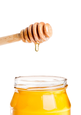 opened honey jar with wooden honey dipper on top with drop honey, isolated on white backgroundの写真素材