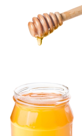 honey jar with wooden honey dipper on top and drop honey, isolated on white backgroundの写真素材