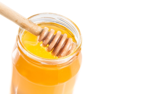 top of view of opened honey jar with wooden honey dipper inside, isolated on white backgroundの写真素材