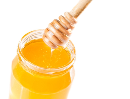 honey jar with wooden honey dipper on top and drop honey, isolated on white backgroundの写真素材