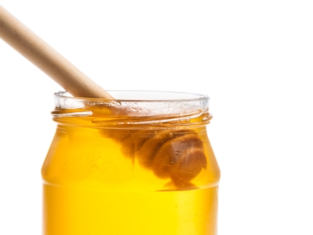 opened honey jar with wooden honey dipper inside, isolated on white backgroundの写真素材