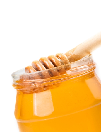 closeup of opened honey jar with wooden honey dipper inside, isolated on white backgroundの写真素材