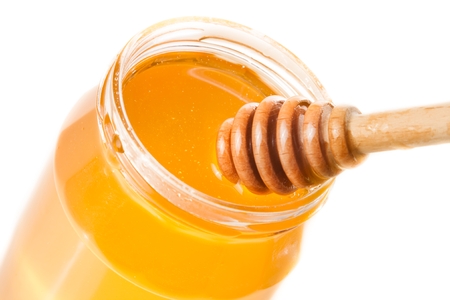 honey jar with wooden honey dipper on top, isolated on white backgroundの写真素材