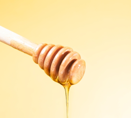 wooden honey dipper with drop honey, isolated on golden backgroundの写真素材