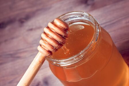 opened honey jar on wood table with honey wooden dipper on topの写真素材