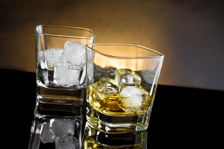whiskey glasses with ice and warm light on black background, with reflectionの写真素材