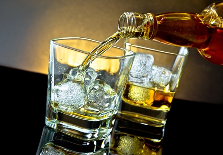 barman pouring whiskey in front of whiskey glass on warm light and black table with reflectionの写真素材