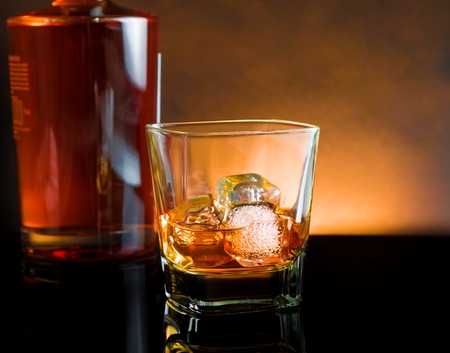 whiskey glass with ice and warm light on black table with reflection, warm atmosphereの写真素材