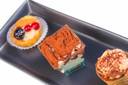 top of view of delicious tiramisu cake near little cakes on black dishの写真素材