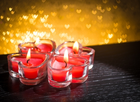 red burning heart shaped candles on golden hearts bokeh backgroundの写真素材