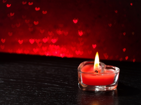 red burning heart shaped candle on red hearts bokeh background, valentine day and love conceptの写真素材