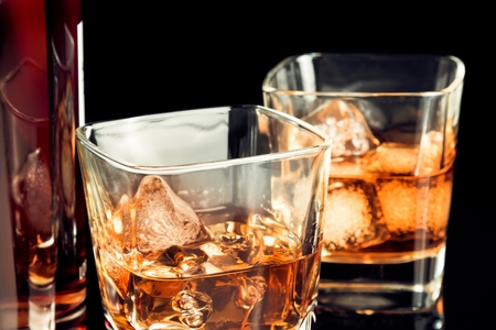 whiskey with ice in glass on black background near bottle, with reflectionの写真素材