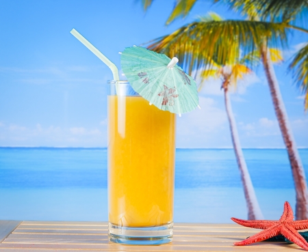 glass of orange juice on the sandy beach near starfish with sea in backgroundの写真素材