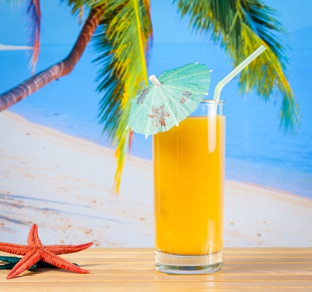 glass of orange juice on the sandy beach near starfish with sea in backgroundの写真素材