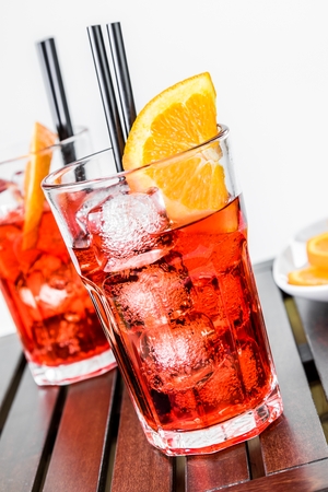 glasses of spritz aperitif aperol cocktail with orange slices and ice cubes near plate of slices oranges on wood tableの写真素材