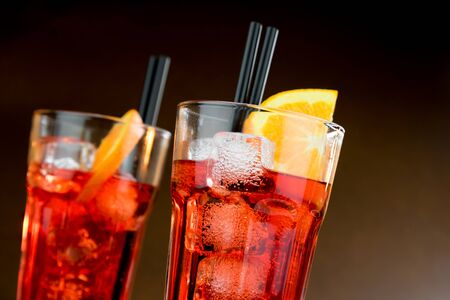 two glasses of spritz aperitif aperol cocktail with orange slices and ice cubes on colored gradient backgroundの写真素材