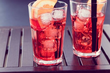 spritz aperitif aperol cocktail with two orange slices and ice cubes on wood table vintage styleの写真素材