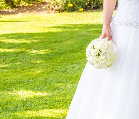 bride holds in hand a wedding bouquet of flowers in a green garden with space for textの写真素材