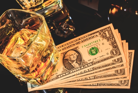 Top of view of glasses of whiskey near bottle on dollars money on a black table. Western theme...