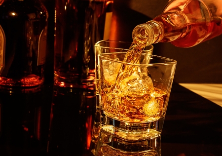 barman pouring whiskey in front of whisky glass and bottles on black tableの写真素材