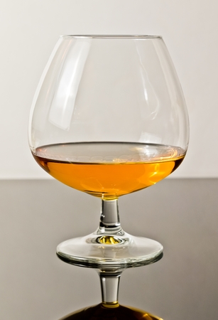 snifter of brandy in elegant typical cognac glass on white light background, with reflectionの写真素材