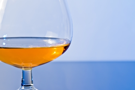 snifter of brandy in elegant typical cognac glass on blue light background, with reflectionの写真素材
