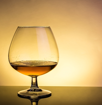 snifter of brandy in elegant typical cognac glass on table with reflection on warm atmosphereの写真素材