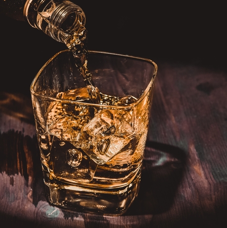 barman pouring whiskey in the glass on wood table, warm atmosphere, old style, time of relax with whisky with space for textの写真素材