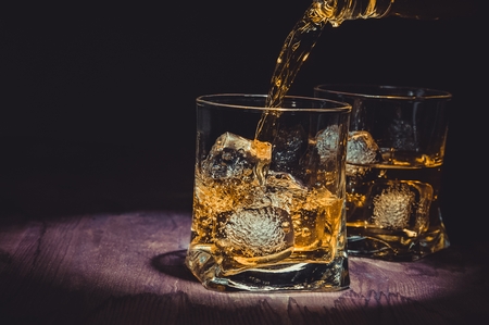 barman pouring whiskey in two glasses on wood table, warm atmosphere, old style, time of relax with whisky with space for textの写真素材