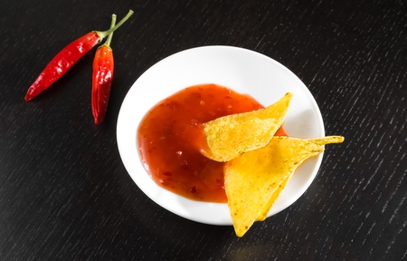 crisp corn nachos with spicy hot tomato sauce as a snack or appetizer in a white disc on black wood tableの写真素材