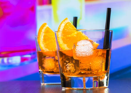 two glasses of spritz aperitif aperol cocktail with orange slices and ice cubes on bar table, disco atmosphere background, lounge bar conceptの写真素材