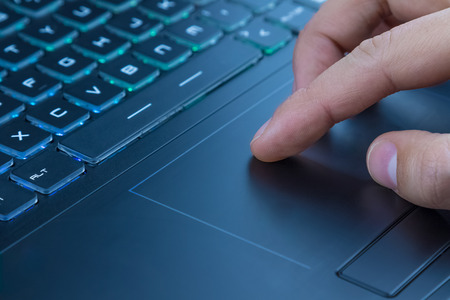 man using touchpad on notebook keyboard with his finger with blue light tint
