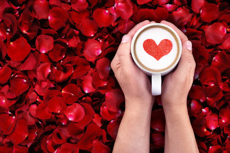 man holding hot cup of milk on red rose petals background, with red heart shape, holiday valentine day love conceptの写真素材