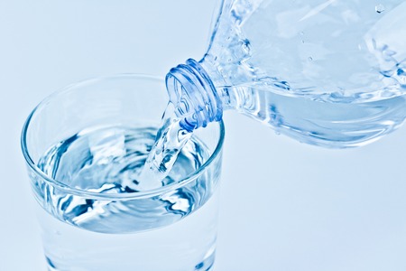 filling a glass with water through bottle, nutrition and health-care concept on white backgroundの写真素材