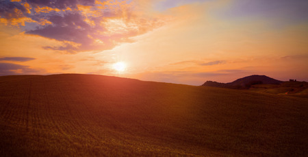 green grass field landscape under sun fall down sunset sky and soft clouds in summer with rural house in the backgroundの写真素材