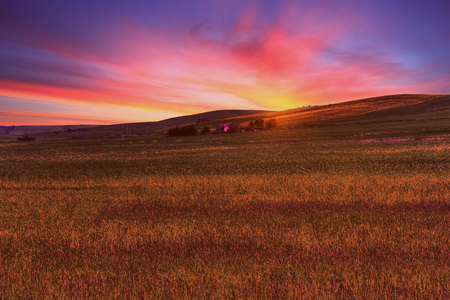 green grass field landscape under sun fall down sunset sky and soft clouds in spring with rural house in the backgroundの写真素材