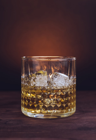 glass of whiskey with ice cubes on wood table, warm atmosphere, time of relax with whiskyの写真素材