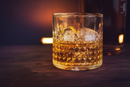 glass of whiskey with ice cubes near bottle on wood table, warm atmosphere, time of relax with whiskyの写真素材