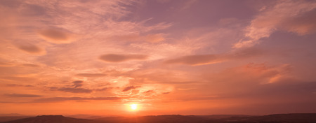 sunset scene with sun fall and ray light, clouds in background, warm colorful sky with soft cloudsの写真素材