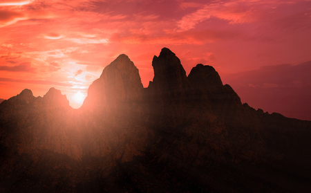 mountains silhouette at sunset scene with sun fall and ray light, clouds in background, warm colorful skyの写真素材