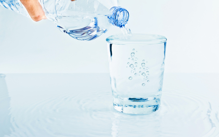 filling a glass with water through bottle, nutrition and health-care concept on white backgroundの写真素材