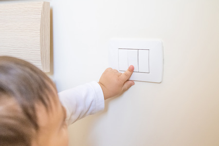 adorable little boy child turning on the white light-switch with his finger of little hand