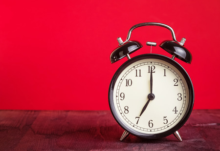 it's seven o'clock already, time to wake up for love, vintage old black metallic alarm clock on red...