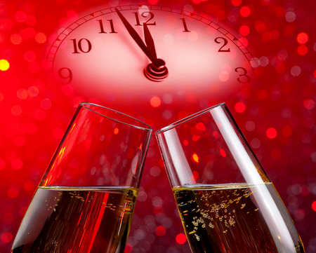champagne flutes with golden bubbles make cheers on red light bokeh background with vintage alarm clock is showing midday or midnight, happy new year conceptの写真素材
