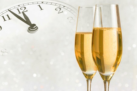 champagne flutes with golden bubbles make cheers on silver light bokeh background with vintage alarm clock is showing midday or midnight, happy new year conceptの写真素材