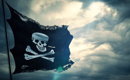 ripped tear grunge old fabric texture of the pirate skull flag waving in wind, calico jack pirate symbol at cloudy sky with sun rays light, dark mystery style, hacker and robber conceptの写真素材