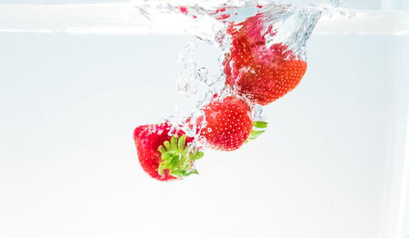 red fresh fruit strawberries falling into water with splash on white background, strawberry for health and diet, nutrition conceptの写真素材
