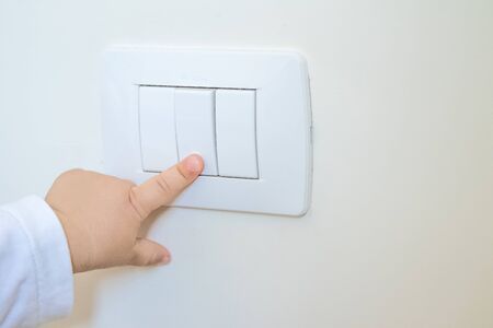 adorable little boy child turning on the white light-switch with his finger of little handの写真素材