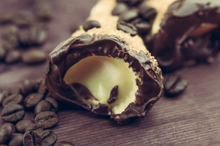 delicious sicilian cannolo cannellino sweet with pastry hazelnut chocolate and pastry cream near coffee beans, italian puff-pastry on wood background, nutrition and diet conceptの写真素材