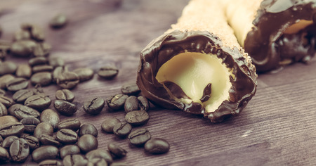 delicious sicilian cannolo cannellino sweet with pastry hazelnut chocolate and pastry cream near coffee beans, italian puff-pastry on wood background, nutrition and diet conceptの写真素材